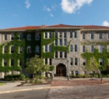 Steele Hall. A 4-story grey brick building with a red roof. The front is covered by windows, and ivy grows over much of the front.